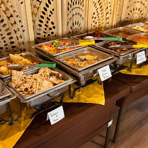 Long buffet table with many chafing dishes containing Indian rice, naan, curries, and fried snacks.