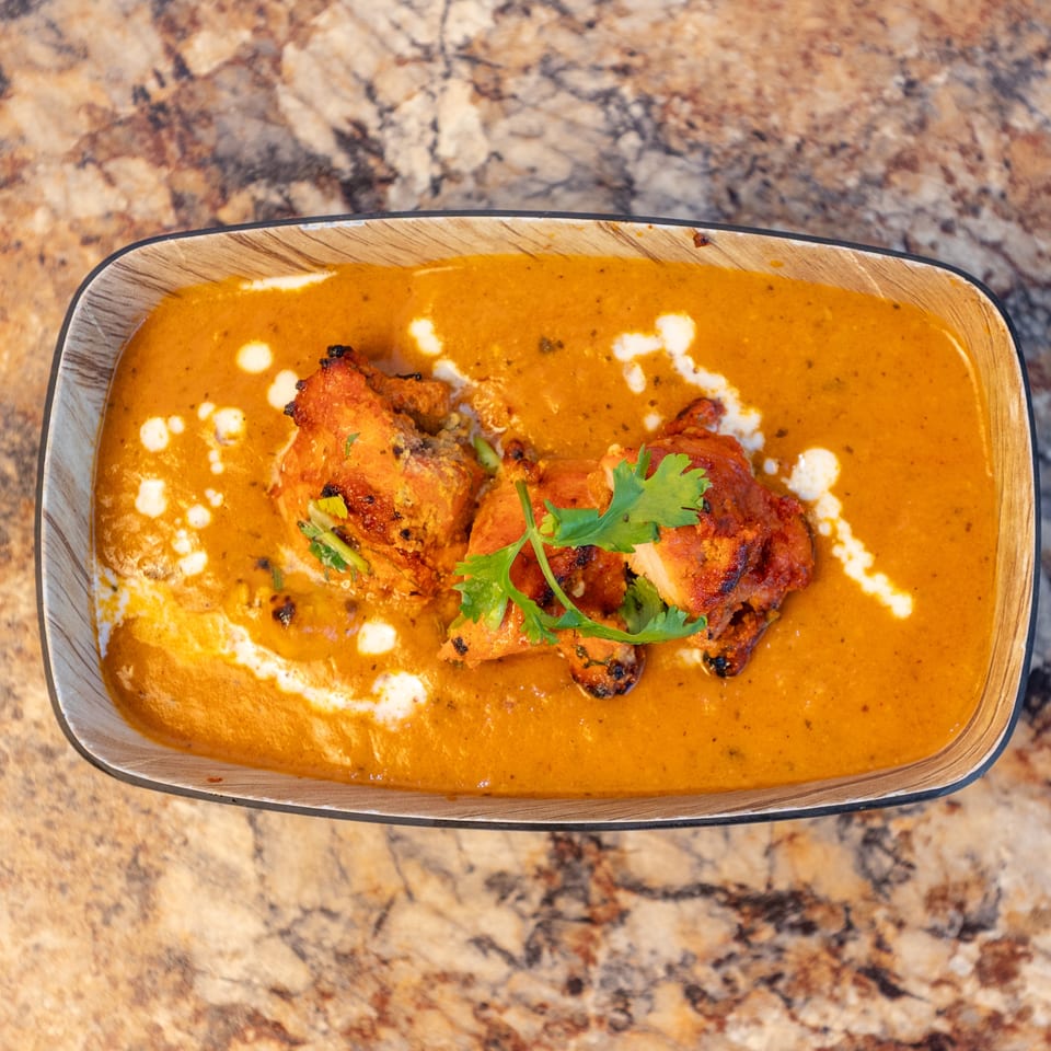 Overhead view of chicken tikka masala with cilantro and cream swirls in a wooden bowl.