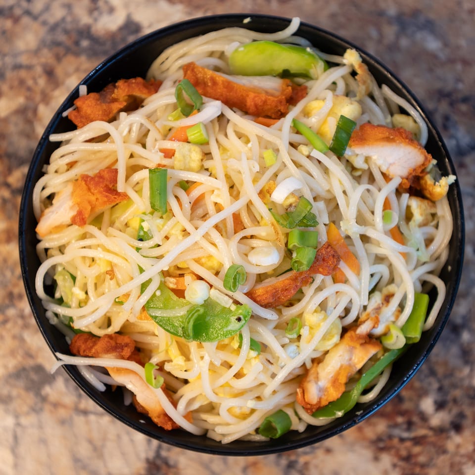 Delicious chicken noodles with mixed vegetables and egg in a black bowl.