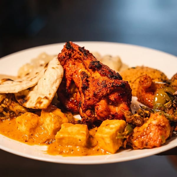 Hand holding a plate of Indian food with tandoori chicken, paneer, and naan.