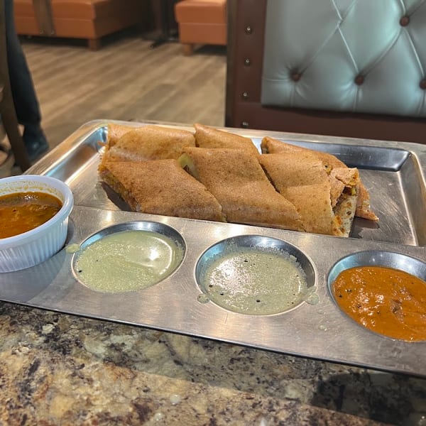 Dosa pieces and four dipping sauces on a metal tray at a restaurant table.