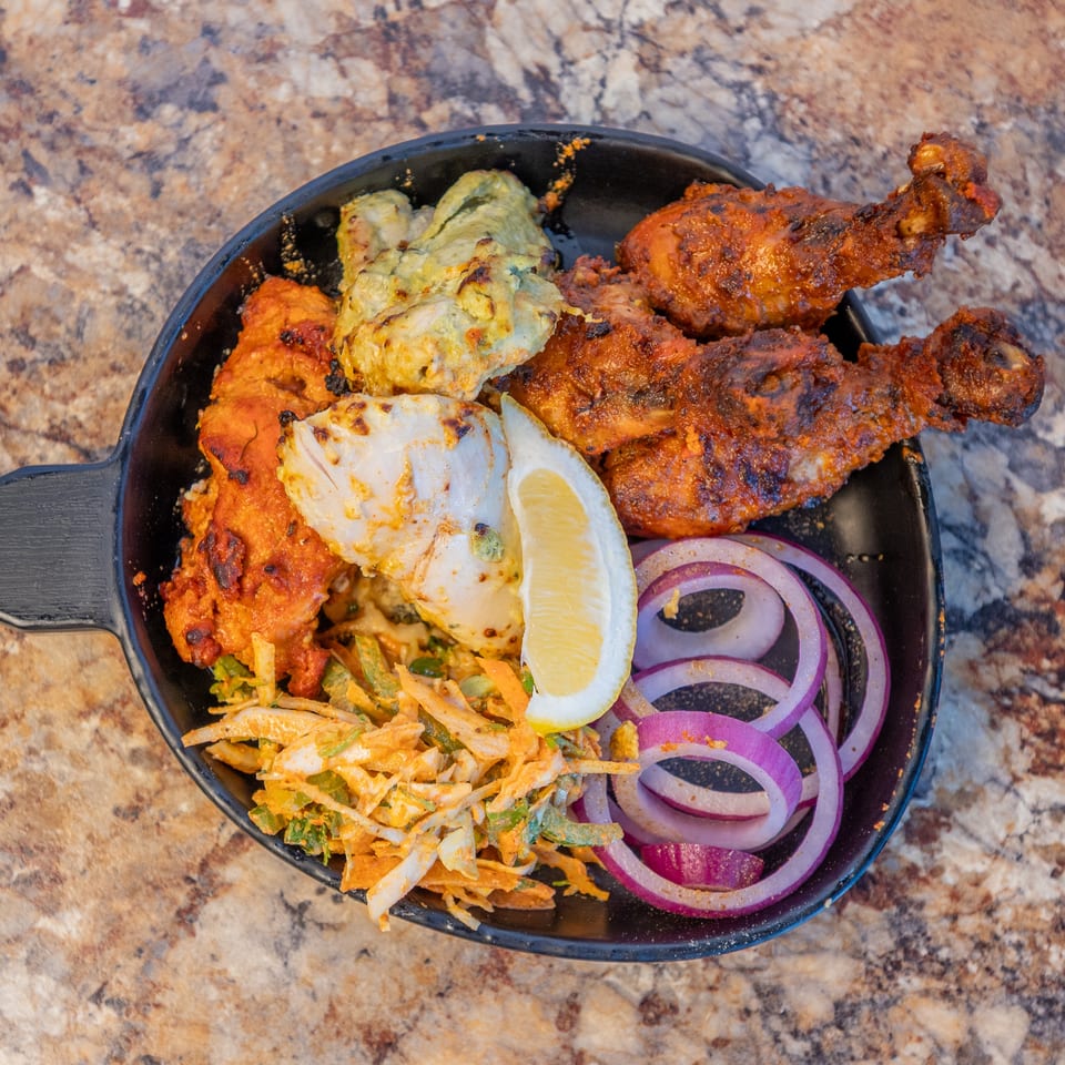 Mixed grilled chicken, lemon, red onion, and slaw served in a black pan.