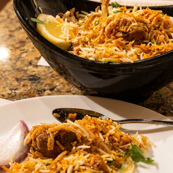 Biryani served in a black bowl and on a white plate with a lemon wedge and red onion.
